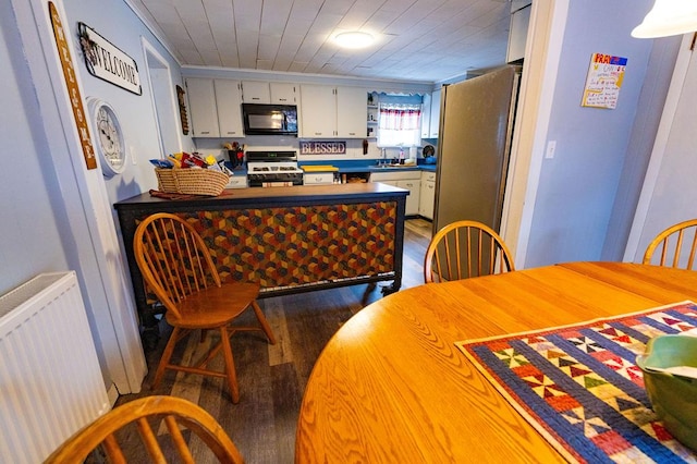 kitchen with stove, dark hardwood / wood-style flooring, stainless steel fridge, white cabinets, and radiator