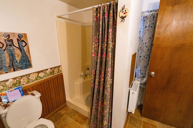 bathroom with radiator heating unit, wooden walls, a shower with shower curtain, and toilet