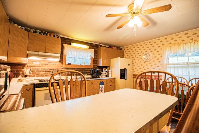 kitchen featuring ceiling fan, white fridge with ice dispenser, and brick wall