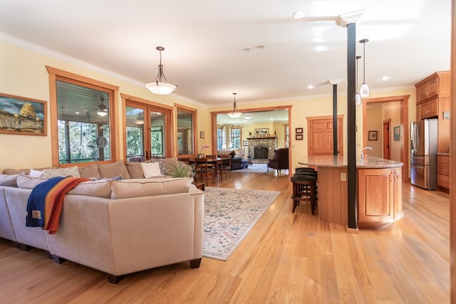 living room with light hardwood / wood-style floors, a stone fireplace, ornate columns, and ornamental molding