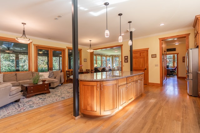 kitchen featuring stainless steel refrigerator, light stone countertops, a healthy amount of sunlight, decorative light fixtures, and light wood-type flooring