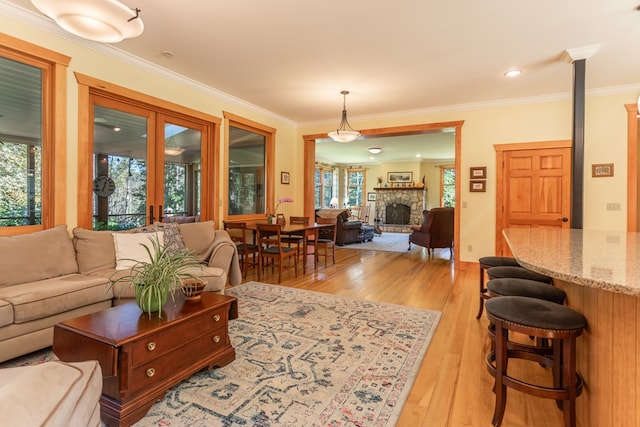 living room featuring a stone fireplace, light hardwood / wood-style flooring, and ornamental molding