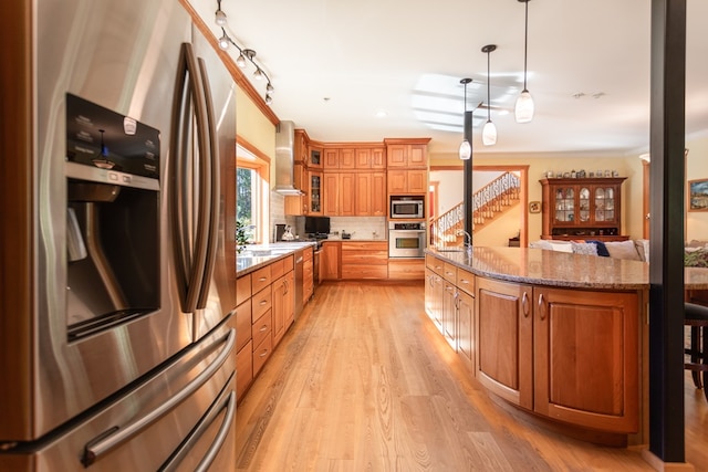 kitchen with tasteful backsplash, dark stone counters, wall chimney exhaust hood, stainless steel appliances, and hanging light fixtures