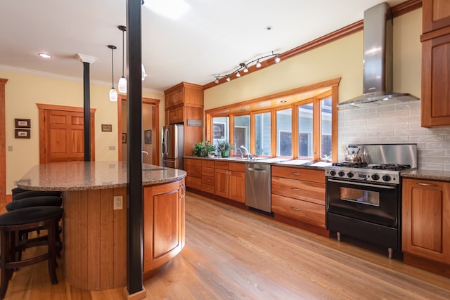 kitchen featuring wall chimney exhaust hood, ornamental molding, light wood-type flooring, tasteful backsplash, and stainless steel appliances