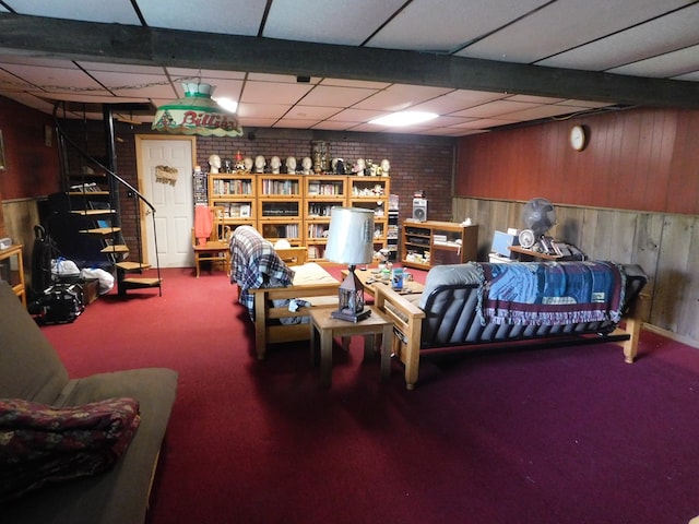 basement with wood walls, a drop ceiling, carpet, and brick wall