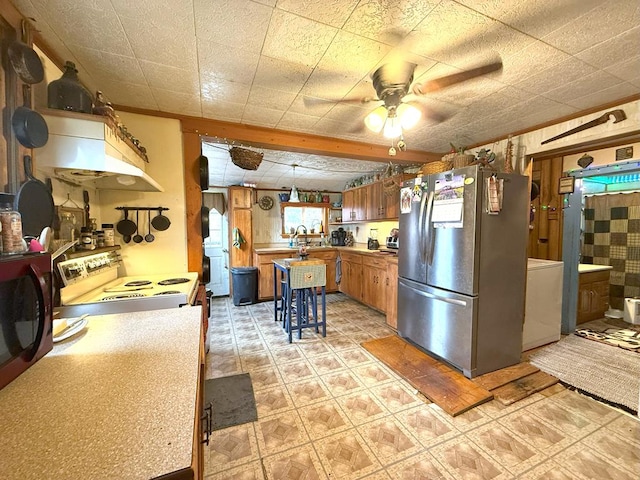 kitchen featuring light floors, light countertops, brown cabinetry, freestanding refrigerator, and a ceiling fan