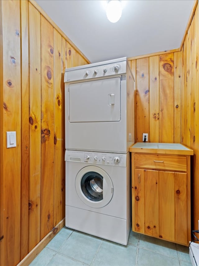 clothes washing area with cabinets, light tile patterned floors, wooden walls, and stacked washer and clothes dryer