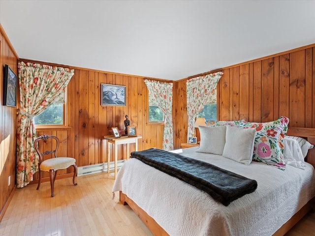 bedroom with wood walls, light wood-type flooring, and a baseboard heating unit