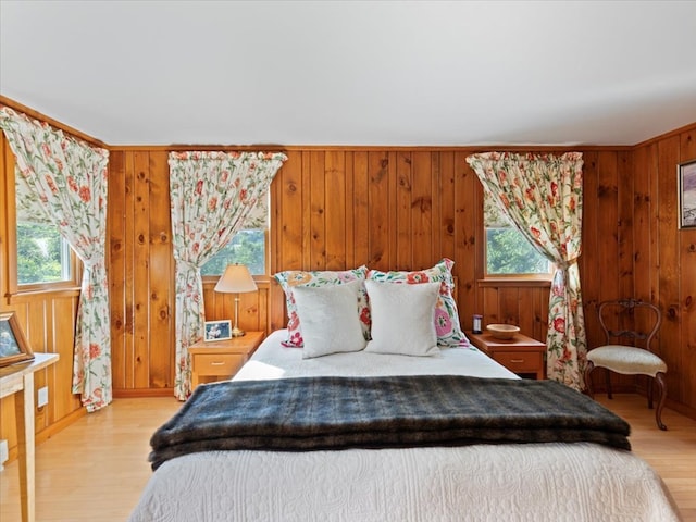 bedroom featuring multiple windows, wooden walls, and light wood-type flooring