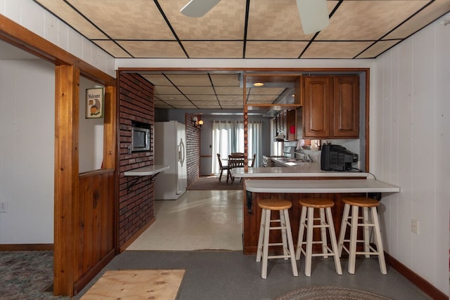 kitchen featuring stainless steel microwave, a kitchen breakfast bar, hanging light fixtures, white refrigerator with ice dispenser, and kitchen peninsula