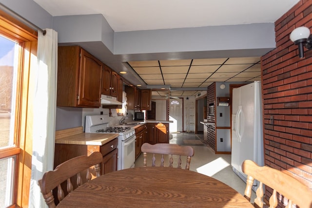 kitchen featuring sink, white appliances, brick wall, a drop ceiling, and kitchen peninsula