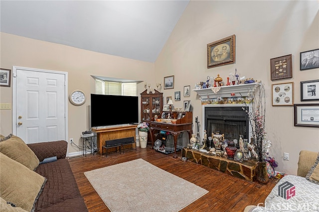 living room featuring a stone fireplace, dark wood-type flooring, and high vaulted ceiling