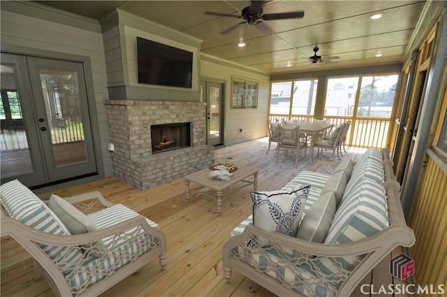 interior space featuring ceiling fan, wooden walls, light hardwood / wood-style floors, a brick fireplace, and french doors