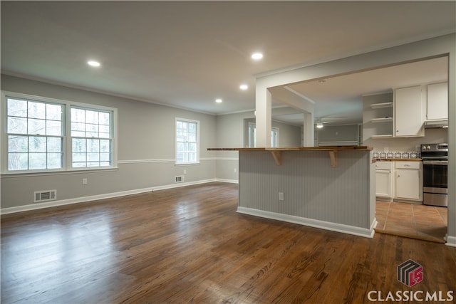 kitchen featuring a kitchen breakfast bar, stove, ornamental molding, dark hardwood / wood-style floors, and white cabinets