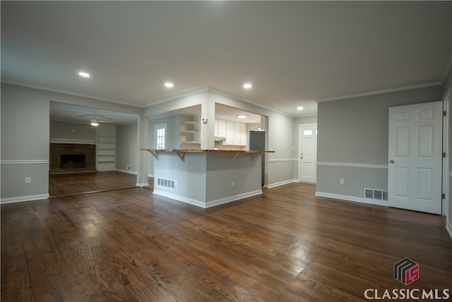 unfurnished living room featuring ceiling fan, a brick fireplace, dark wood-type flooring, and crown molding