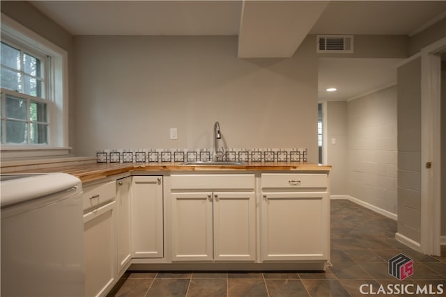 kitchen featuring white cabinets, butcher block countertops, dark tile flooring, and sink