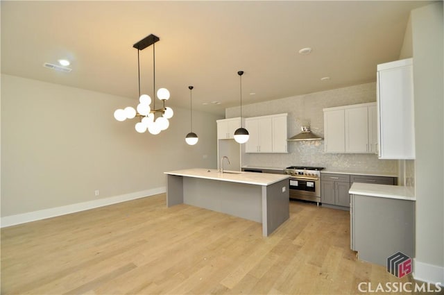 kitchen featuring decorative backsplash, high end stainless steel range oven, sink, white cabinets, and hanging light fixtures