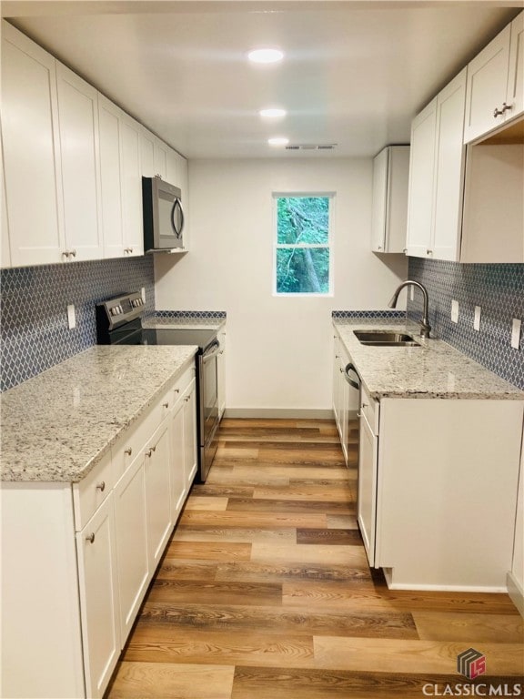 kitchen with white cabinets, appliances with stainless steel finishes, sink, tasteful backsplash, and light hardwood / wood-style floors