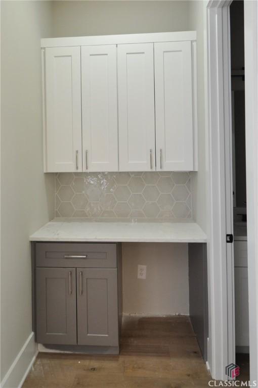 kitchen with white cabinets, dark hardwood / wood-style floors, built in desk, and backsplash