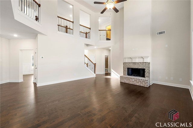 unfurnished living room featuring dark hardwood / wood-style floors, a fireplace, ceiling fan, and a high ceiling