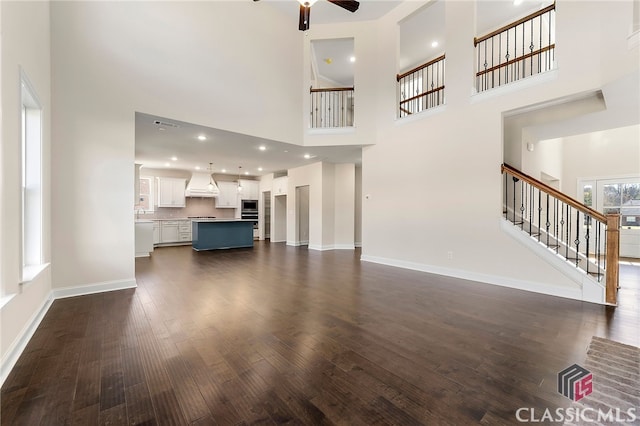 unfurnished living room featuring dark hardwood / wood-style floors, ceiling fan, a towering ceiling, and sink