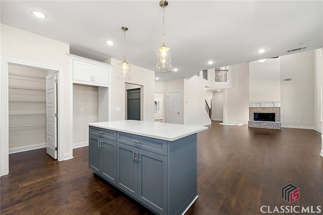 kitchen featuring a brick fireplace, a kitchen island, white cabinetry, dark wood-type flooring, and decorative light fixtures