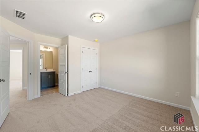 unfurnished bedroom with light colored carpet, ensuite bath, and a closet