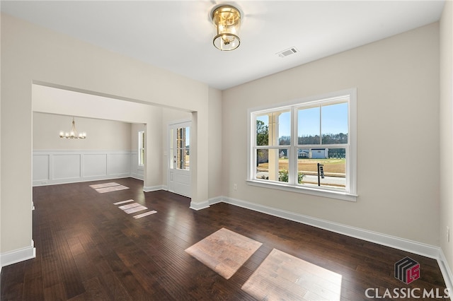 spare room featuring dark wood-type flooring and an inviting chandelier