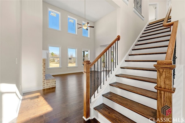 stairs with a towering ceiling, dark hardwood / wood-style flooring, and ceiling fan