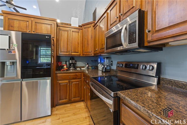 kitchen featuring appliances with stainless steel finishes, dark stone countertops, light wood-type flooring, and ceiling fan