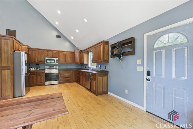 kitchen featuring high vaulted ceiling, appliances with stainless steel finishes, sink, and light hardwood / wood-style floors