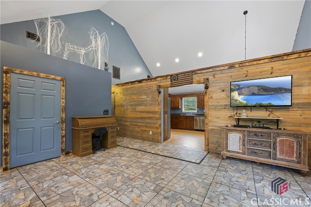 unfurnished living room with a barn door, high vaulted ceiling, wooden walls, and light tile floors