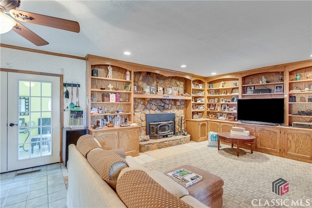 tiled living room featuring a stone fireplace, a wealth of natural light, built in shelves, and ceiling fan