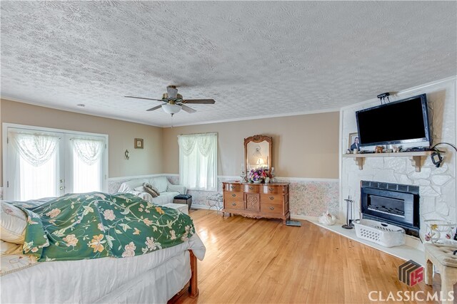 bedroom featuring ceiling fan, a stone fireplace, a textured ceiling, wood-type flooring, and french doors