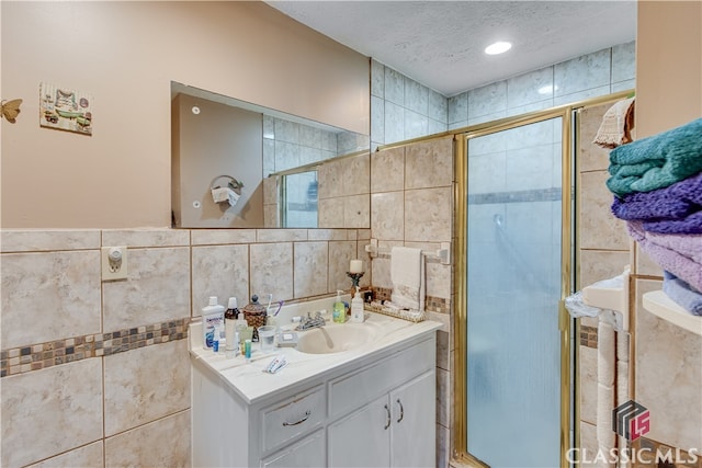 bathroom featuring a shower with door, tile walls, a textured ceiling, and vanity