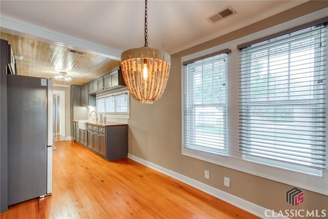 kitchen with a healthy amount of sunlight, sink, stainless steel refrigerator, light wood-type flooring, and gray cabinetry