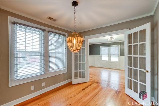 unfurnished dining area with crown molding, hardwood / wood-style flooring, an inviting chandelier, and french doors