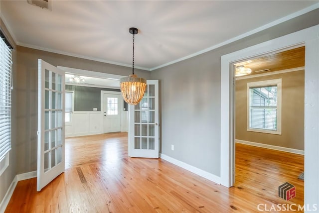 unfurnished dining area with crown molding, hardwood / wood-style floors, a notable chandelier, and french doors