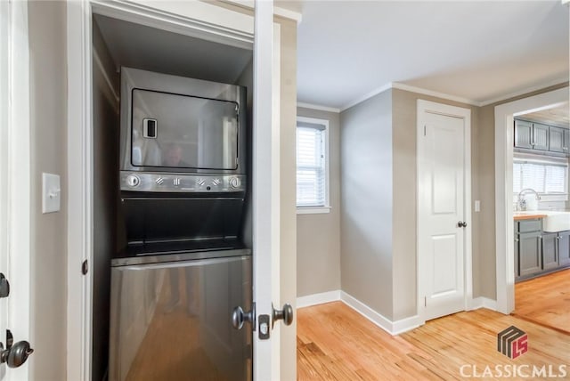 washroom featuring sink, hardwood / wood-style floors, ornamental molding, and stacked washing maching and dryer