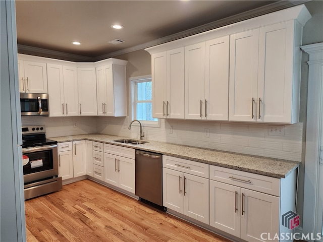 kitchen with light hardwood / wood-style floors, stainless steel appliances, white cabinets, sink, and tasteful backsplash