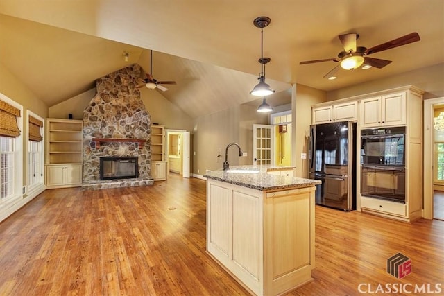 kitchen featuring light stone countertops, black appliances, decorative light fixtures, a stone fireplace, and sink