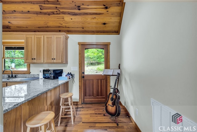 kitchen with a healthy amount of sunlight, light stone counters, light wood-style floors, black microwave, and a kitchen breakfast bar