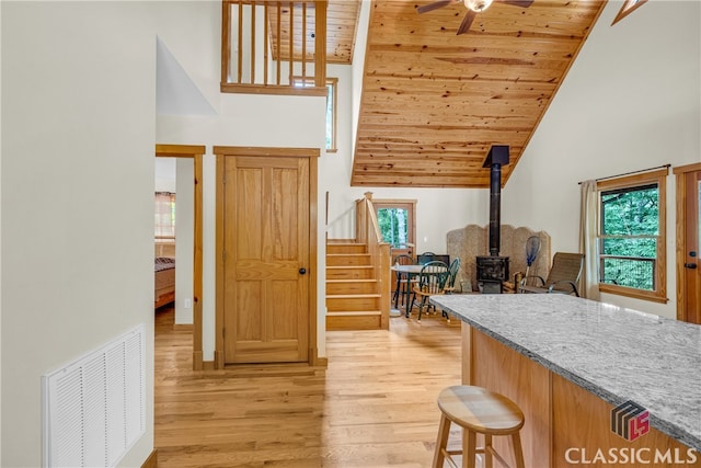 kitchen featuring a wood stove, light wood finished floors, high vaulted ceiling, a wealth of natural light, and visible vents