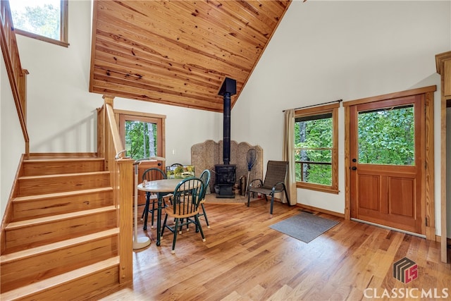 entryway featuring light wood-style flooring, a wood stove, stairway, baseboards, and high vaulted ceiling