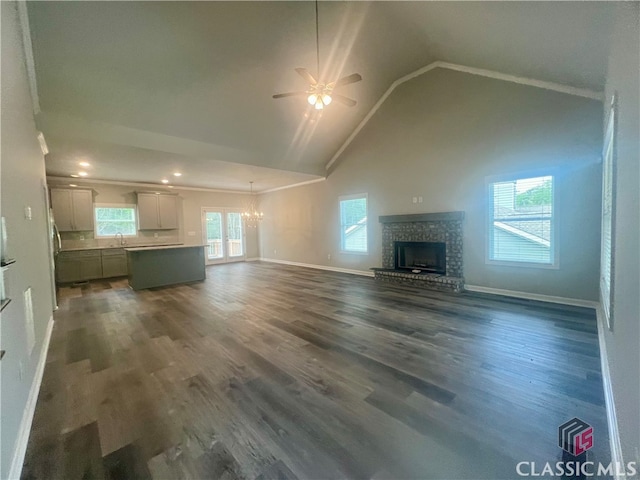 unfurnished living room featuring high vaulted ceiling, a brick fireplace, ceiling fan with notable chandelier, and hardwood / wood-style floors