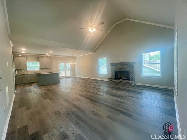 unfurnished living room with a fireplace, dark hardwood / wood-style flooring, ceiling fan with notable chandelier, high vaulted ceiling, and sink