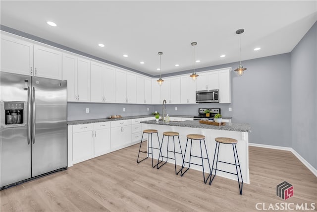 kitchen with pendant lighting, stainless steel appliances, white cabinetry, and light hardwood / wood-style floors