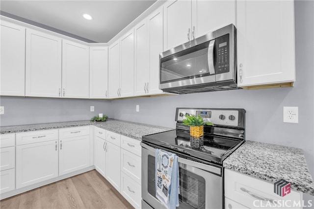 kitchen with white cabinets, appliances with stainless steel finishes, light hardwood / wood-style flooring, and light stone countertops