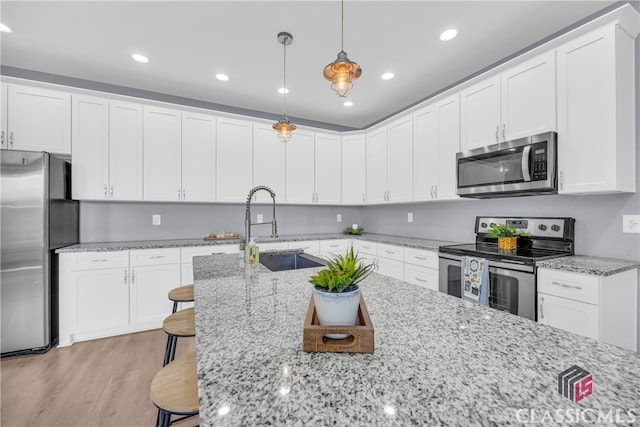 kitchen with a breakfast bar, stainless steel appliances, sink, light hardwood / wood-style floors, and hanging light fixtures