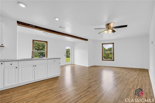 unfurnished living room featuring beamed ceiling, light wood-type flooring, ceiling fan, and sink